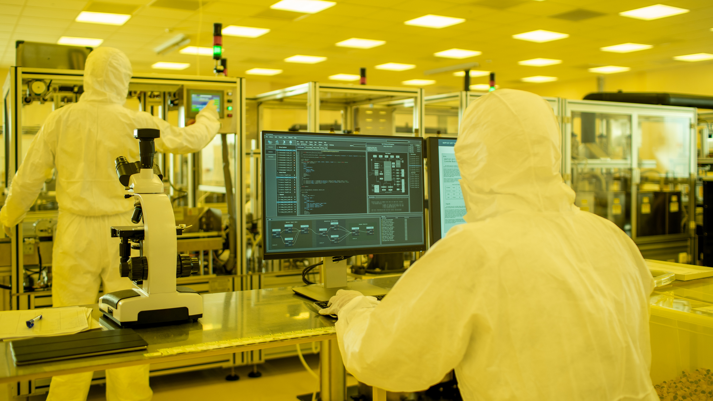 Shot of a Scientists in Sterile Suits Working with Computers, Analyzing Data form Modern Industrial Machinery in the Laboratory. Product Manufacturing Process: Pharmaceutics, Semiconductors, Biotechnology.